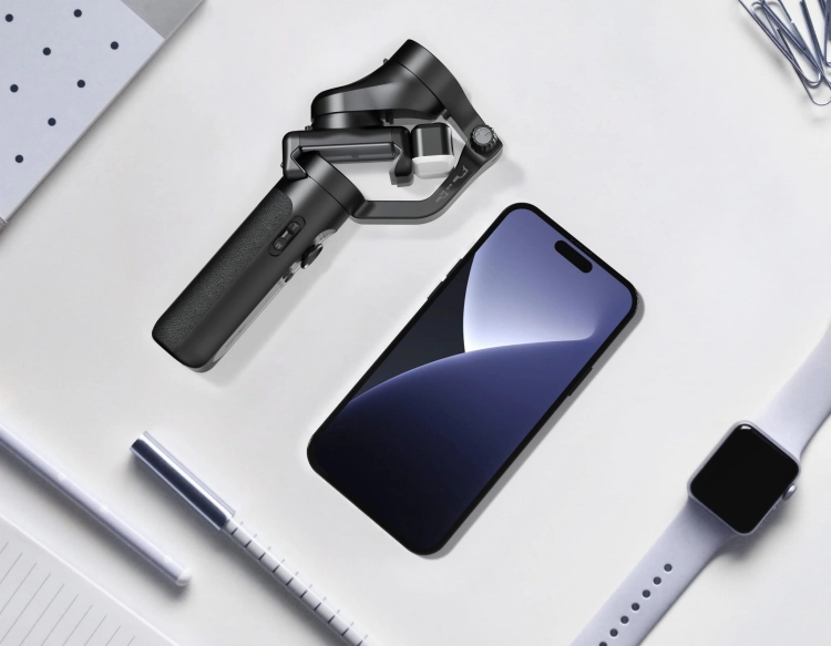 Gimbal Hohem iSteady XE Kit czarny złożony obok smartfona i zegarka na biurku – porównanie rozmiaru