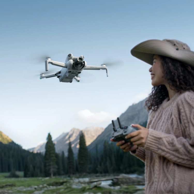 Kobieta w kapeluszu steruje dronem DJI Mini 4 Pro w górskiej dolinie