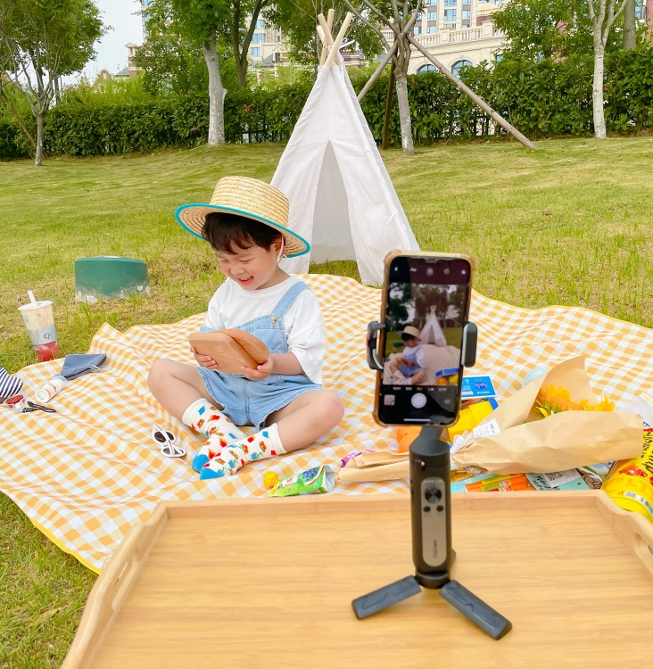 Gimbal Hohem iSteady X2 czarny na statywie ze smartfonem nagrywającym dziecko na pikniku