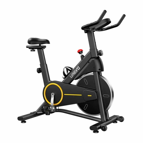 Kobieta w sportowym stroju stojąca obok czarnego roweru stacjonarnego UREVO T1 w domowym salonie.