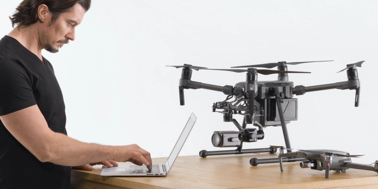 Technik przy laptopie obok dronów DJI Matrice i Mavic Enterprise podczas diagnostyki serwisowej
