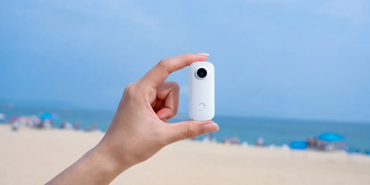 Kamera SJCAM C100 Pro trzymana w dwóch palcach na tle plaży