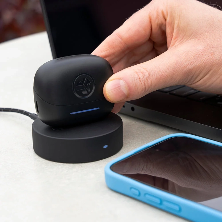 Etui JLab JBuds Pods ANC na ładowarce bezprzewodowej obok telefonu