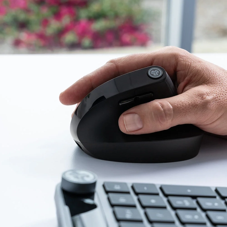 Dłoń na pionowej myszy JLab JBuds Ergonomic obok klawiatury