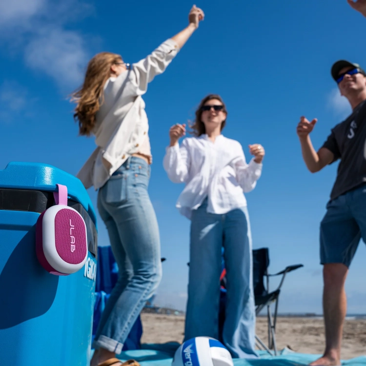 Grupa przyjaciół tańczy na plaży przy głośniku JLab Pop Party