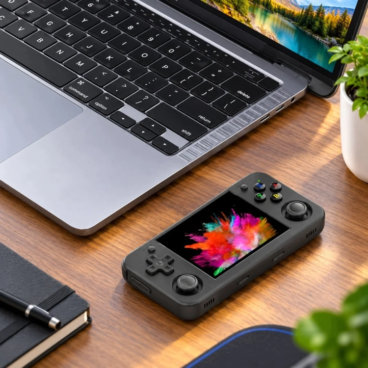 ANBERNIC RG35XX H obok laptopa na biurku, mała konsola do pracy i podróży
