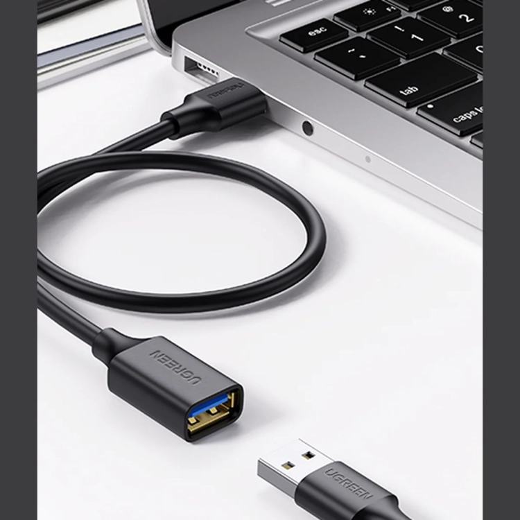 Przedłużacz UGREEN US129 wpięty w laptop, obok wtyk urządzenia USB