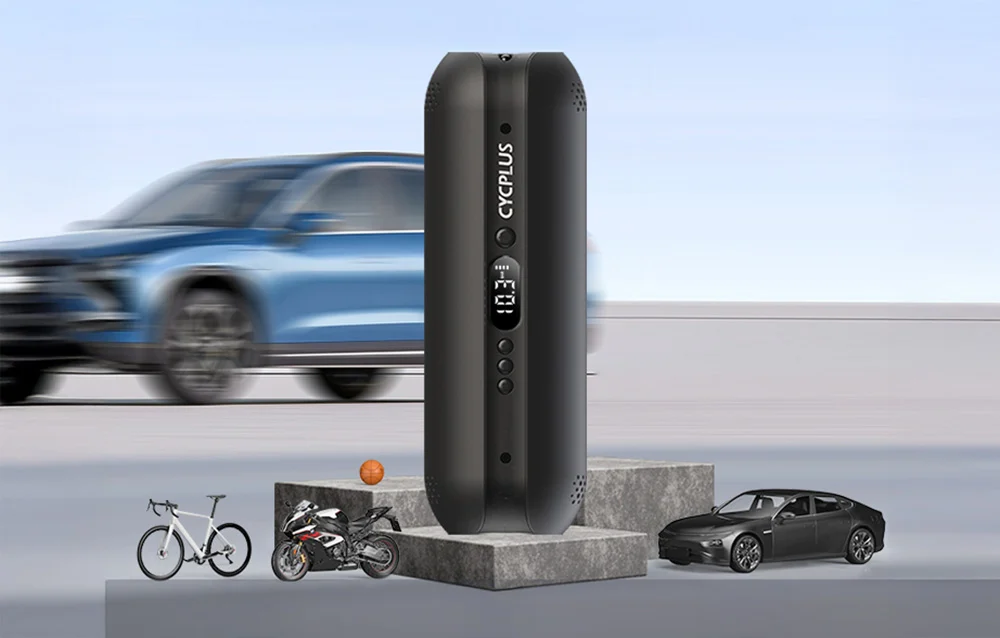 Pompka elektryczna Cycplus A2 Plus stojąca pionowo na betonowych kostkach z rozmytym samochodem w tle.