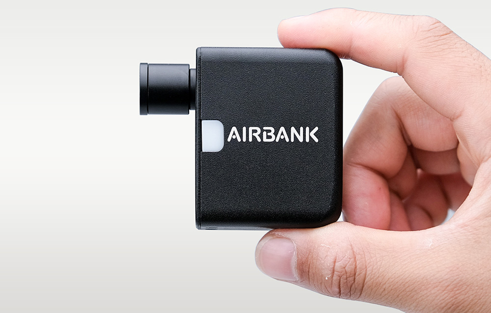 Czarna mini pompka rowerowa z napisem Airbank trzymana w dwóch palcach dłoni na jasnym tle.