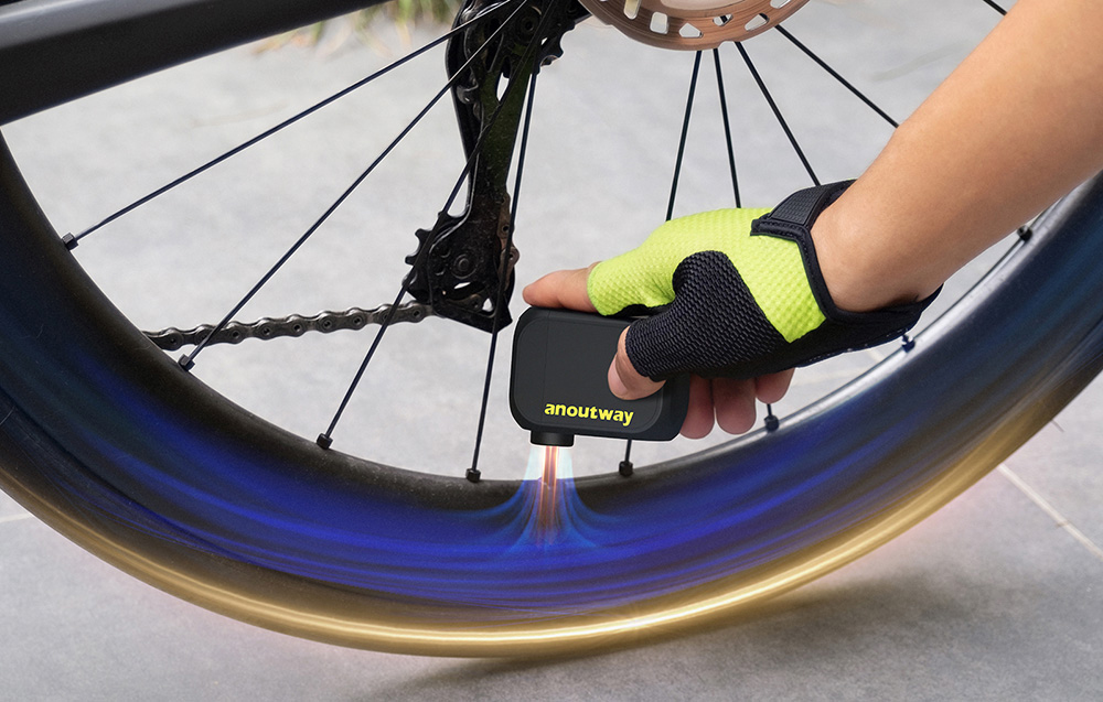 Dłoń w rękawiczce przykłada czarną mini pompkę Cycplus bezpośrednio do wentyla koła roweru szosowego.