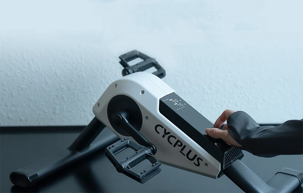 Dłoń użytkownika precyzyjnie regulująca parametry oporu pracy za pomocą pokrętła na rowerze Cycplus.