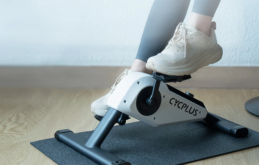 Stopy osoby siedzącej swobodnie pedałujące w przód i tył na mini rowerze rehabilitacyjnym.