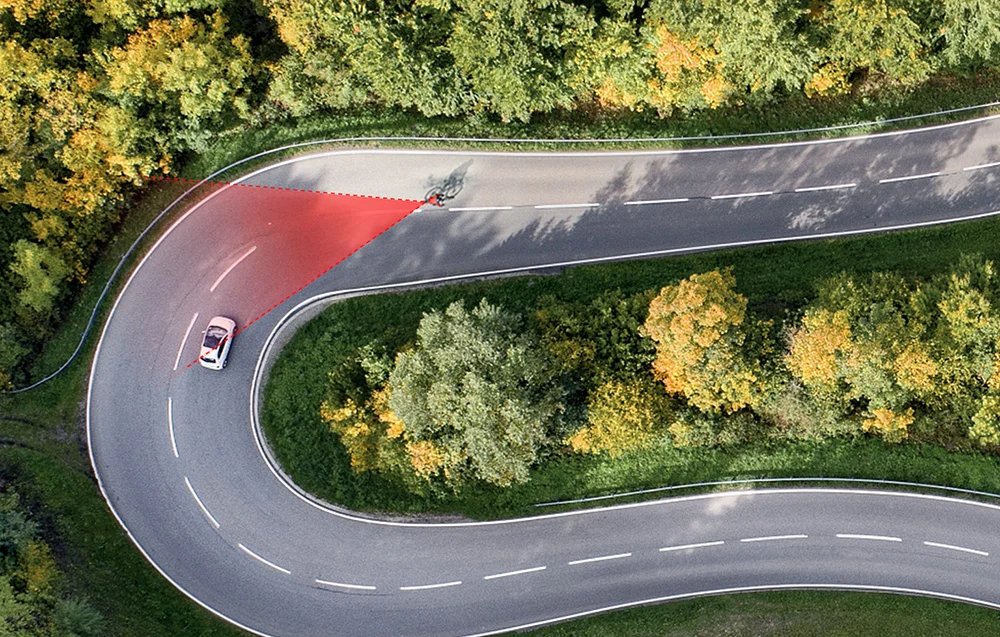 Rzut z lotu ptaka na rowerzystę w zakręcie z zaznaczoną czerwoną strefą szerokiego kąta detekcji radaru.