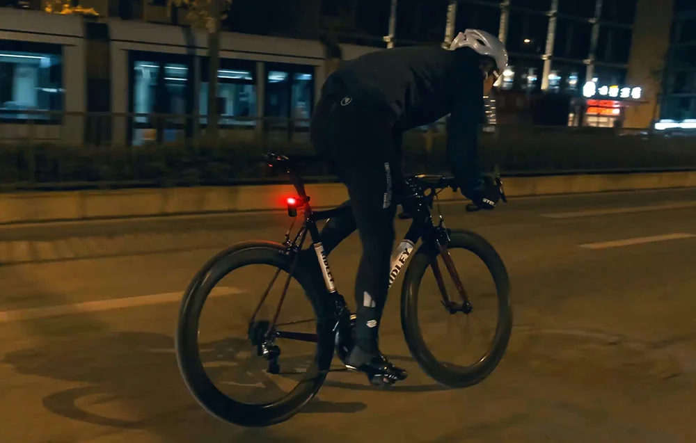 Rowerzysta jadący nocą po mieście oświetlany intensywnym czerwonym światłem z lampki radarowej Cycplus.