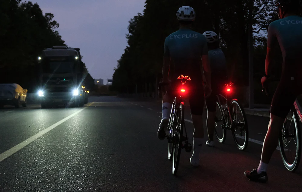 Grupa trzech rowerzystów jadących w peletonie ze zsynchronizowanymi lampkami ostrzegawczymi.