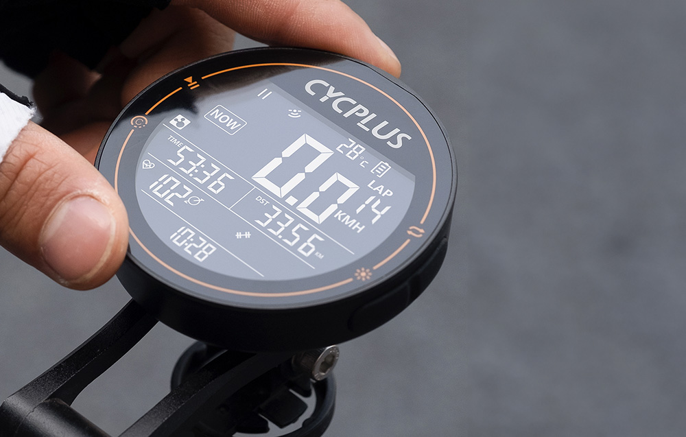 Nowoczesny, okrągły komputer rowerowy Cycplus M2 zamontowany na kierownicy wyścigowego roweru szosowego.