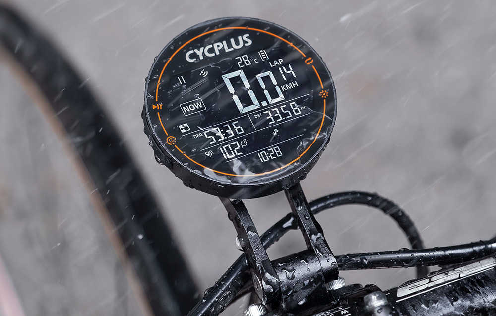 Dłoń trzymająca komputer rowerowy Cycplus M2 z czytelnym wyświetlaczem prezentującym aktualną prędkość i dystans.