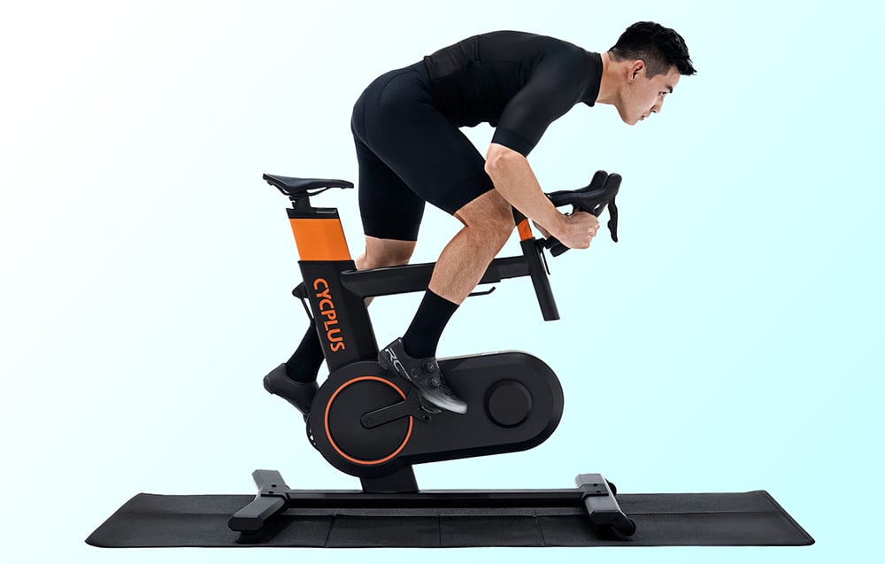 Mężczyzna wykonujący intensywny trening na czarno-pomarańczowym rowerze stacjonarnym Cycplus T7.