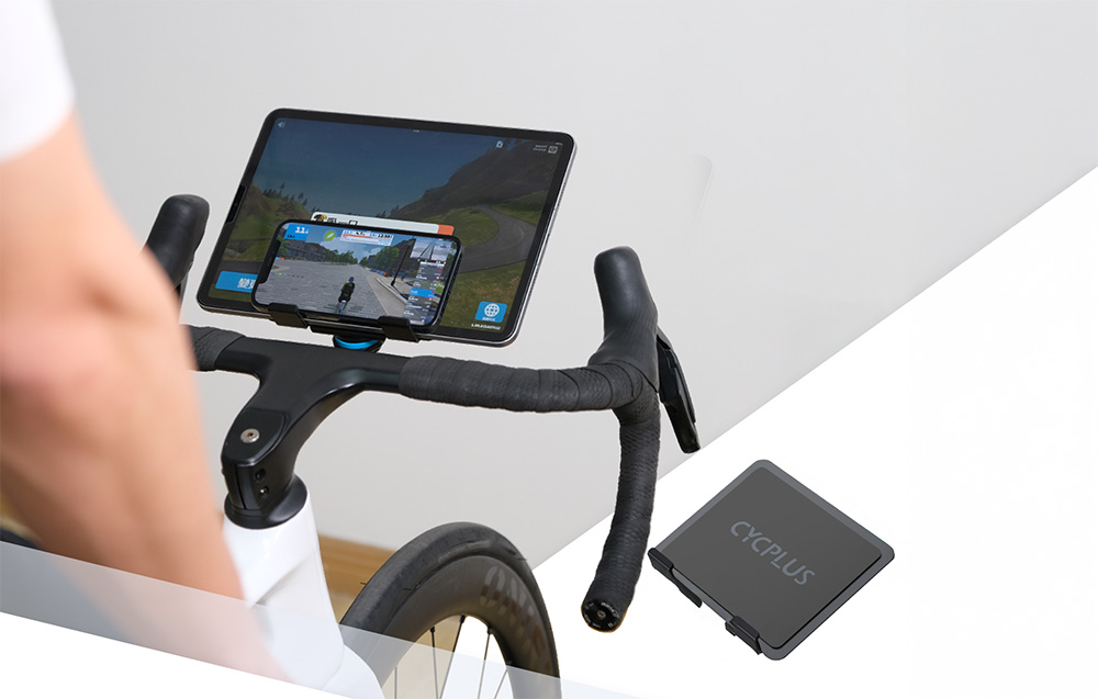 Duży tablet z uruchomioną wirtualną aplikacją treningową stabilnie zamocowany na kierownicy roweru stacjonarnego.