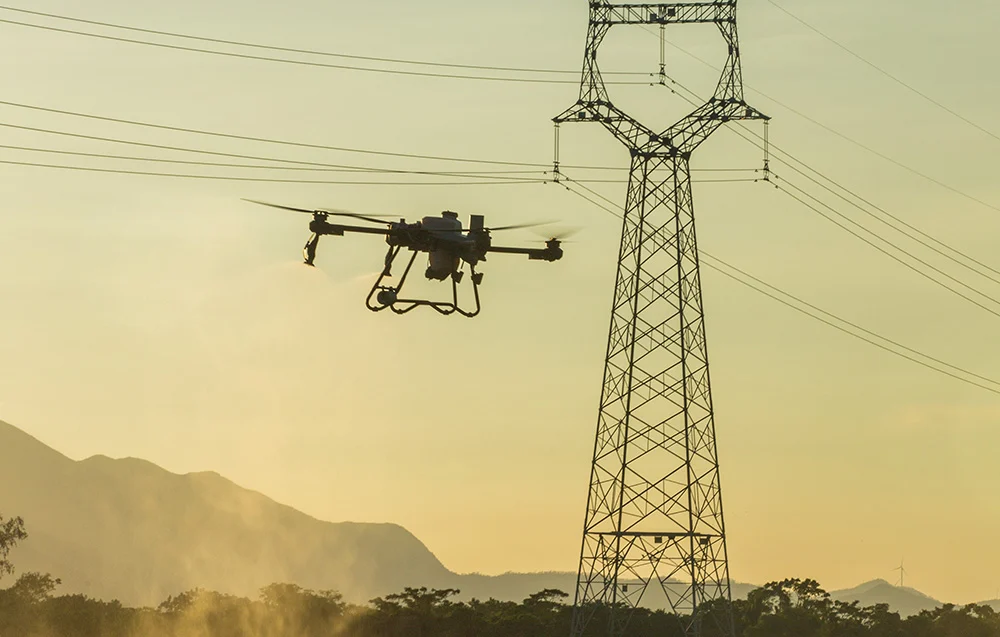 DJI Agras T25P w locie obok linii energetycznych – praca w złożonym terenie i wymóg bezpieczeństwa.