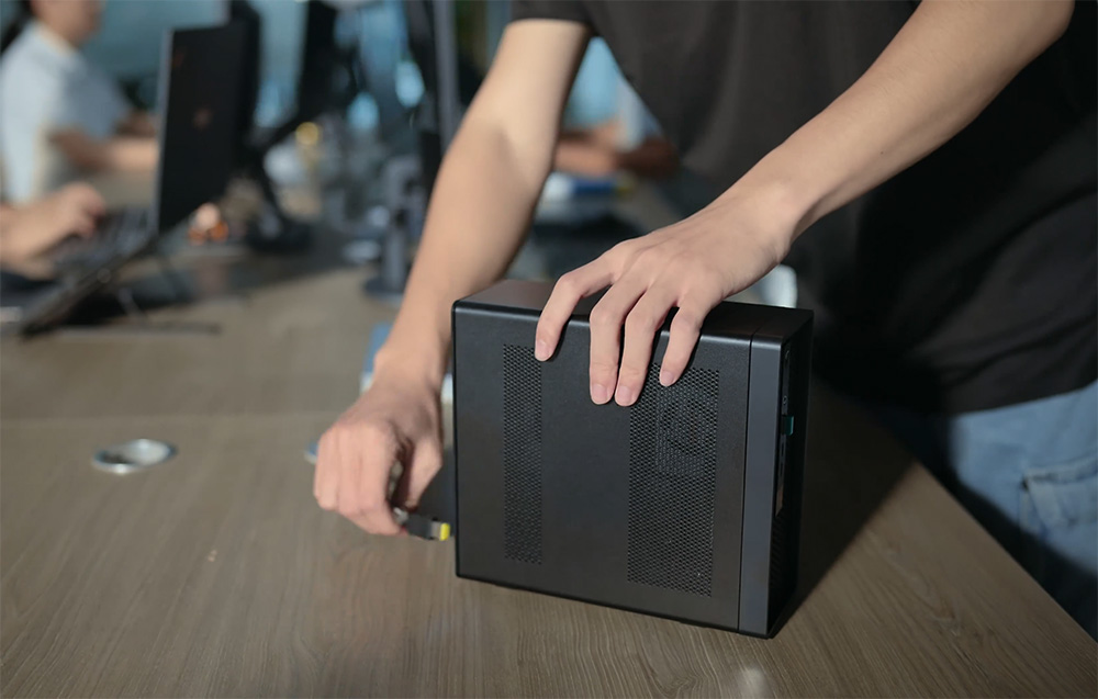 Dłonie ustawiające kompaktową obudowę stacji roboczej na biurku w biurze