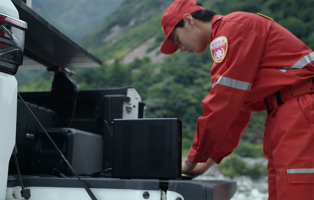 Osoba w czerwonym kombinezonie obsługująca sprzęt na pace pickupa w górach