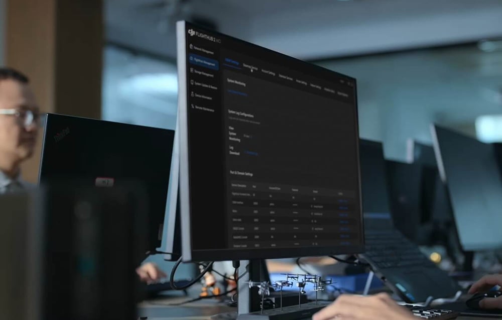 Monitor z interfejsem FlightHub 2 w biurze obok osób pracujących przy biurkach