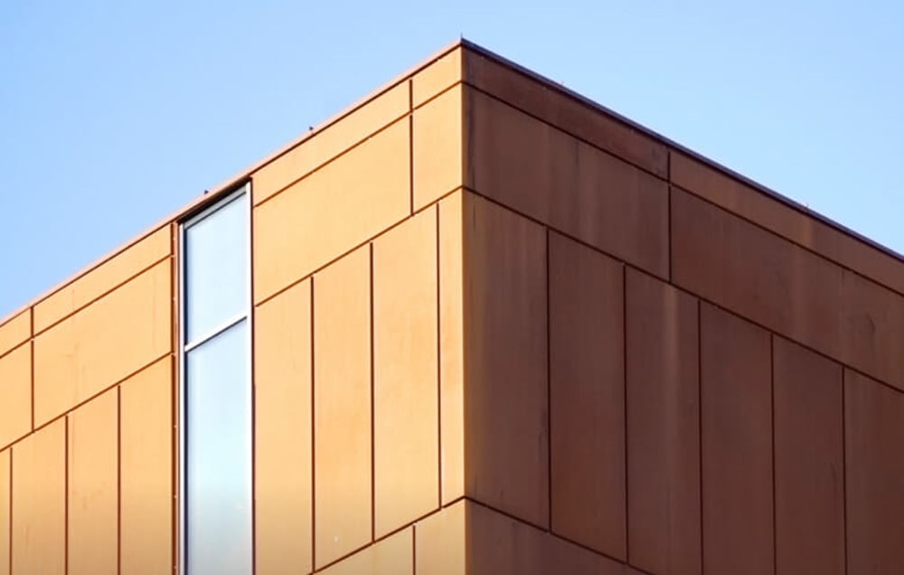 róg nowoczesnego budynku z pomarańczową elewacją i pionowym oknem, na tle nieba