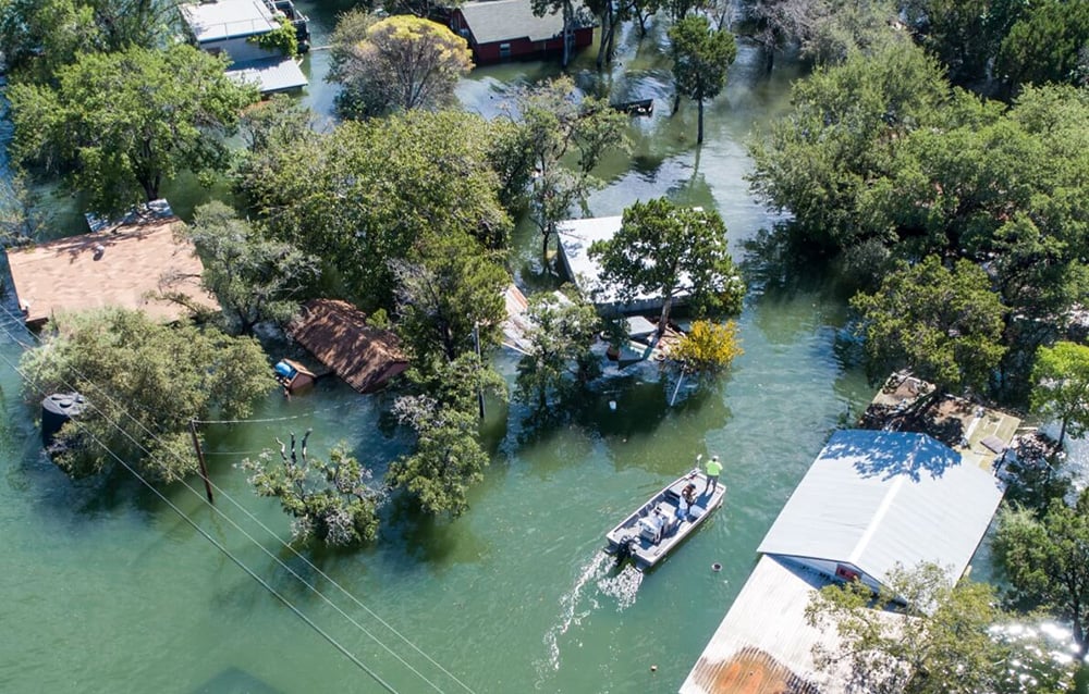 zalane osiedle z domami i drzewami częściowo pod wodą oraz łodzią z ludźmi