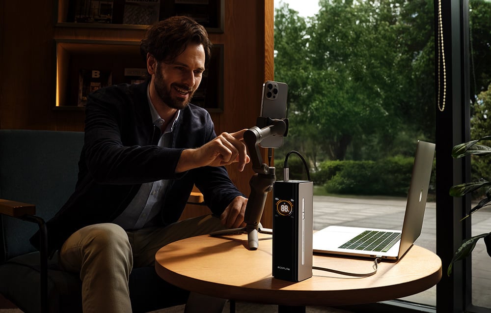 Uśmiechnięty mężczyzna z brodą używa gimbala ze smartfonem w domu przy oknie