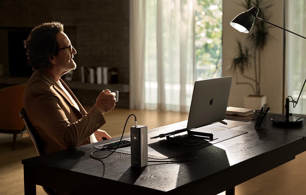 mężczyzna w okularach pije kawę przy biurku z laptopem i lampą biurkową w jasnym pokoju