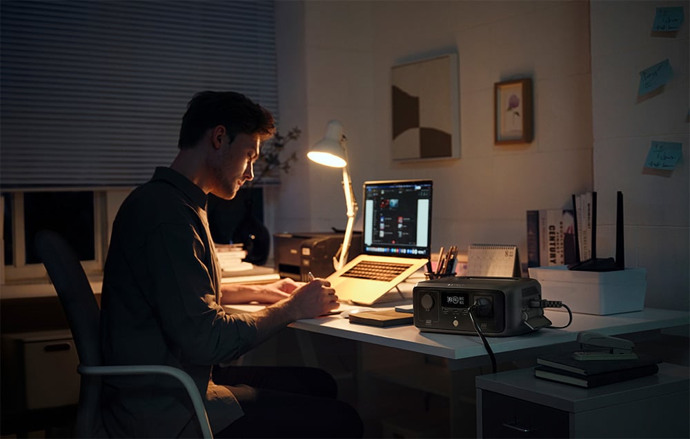 Mężczyzna pracujący przy biurku z laptopem i stacją zasilania EcoFlow RIVER 3 UPS zasilającą lampkę