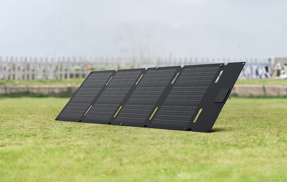 Składany panel fotowoltaiczny rozłożony na trawie na tle ogrodzenia