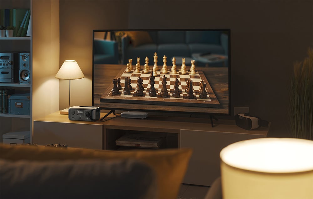 Stacja EcoFlow RIVER 3 UPS obok lampki i telewizora wyświetlającego szachownicę w przytulnym salonie
