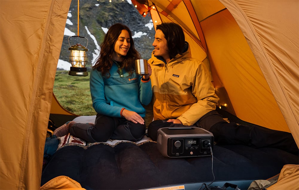 Para siedząca w namiocie z lampką i stacją EcoFlow RIVER 3 UPS na materacu