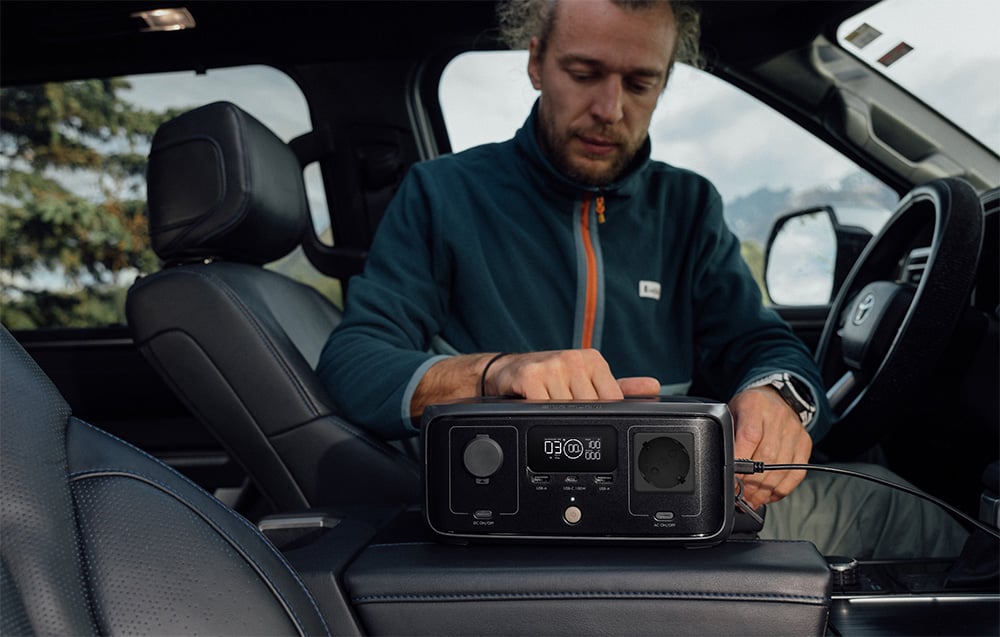 Mężczyzna w aucie obsługujący stację EcoFlow RIVER 3 UPS ustawioną na podłokietniku