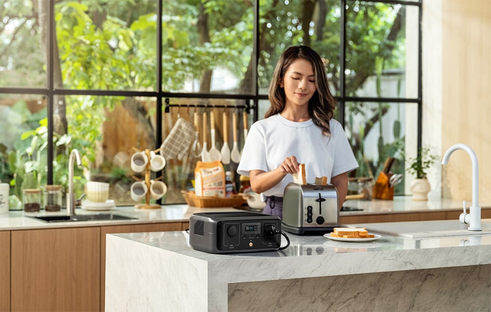 Kobieta w kuchni wkładająca kromkę chleba do tostera zasilanego przez stację EcoFlow RIVER 3 UPS