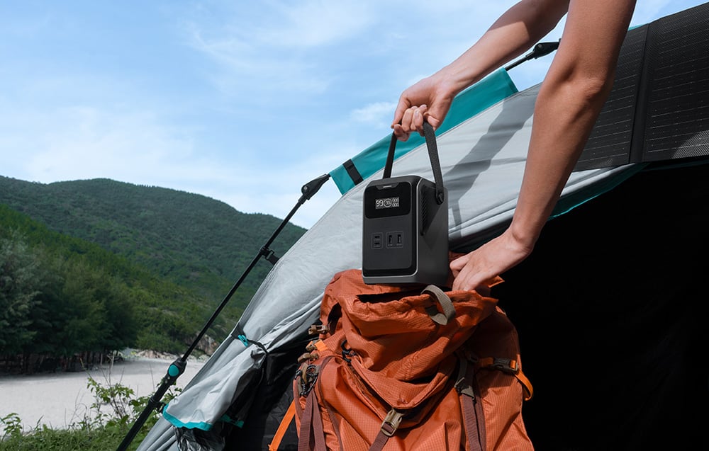 Ręce umieszczają EcoFlow TRAIL 200 DC na plecaku przed namiotem nad jeziorem