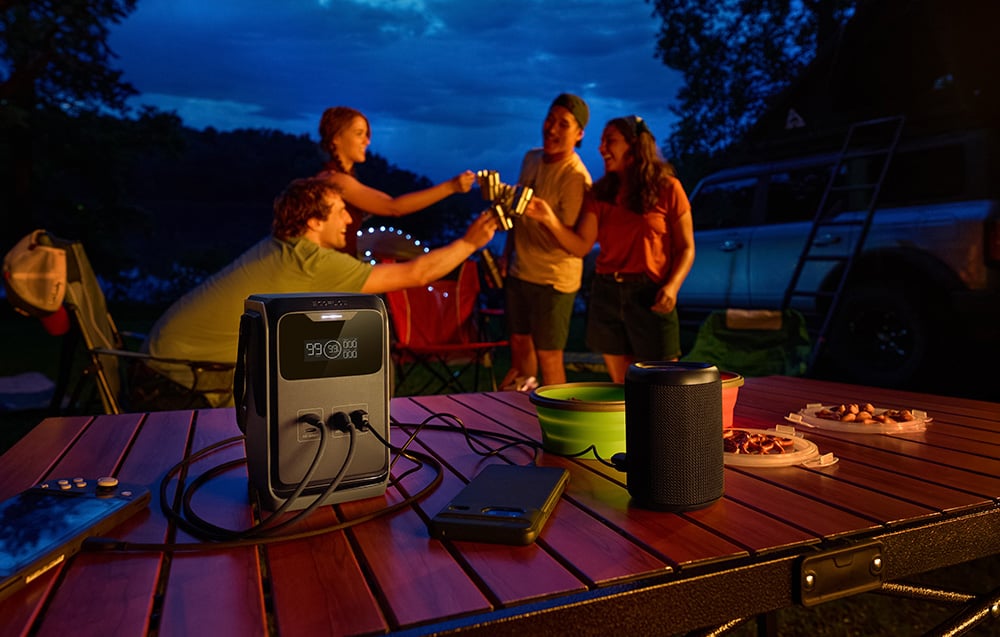 EcoFlow TRAIL 200 DC na stole kempingowym obok głośnika i urządzeń elektronicznych wieczorem