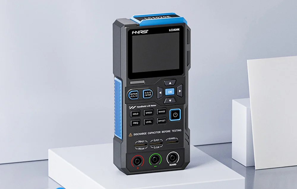 Nowoczesny, ręczny miernik LCR FNIRSI LC1020E stojący stabilnie na czarnym biurku laboratoryjnym.