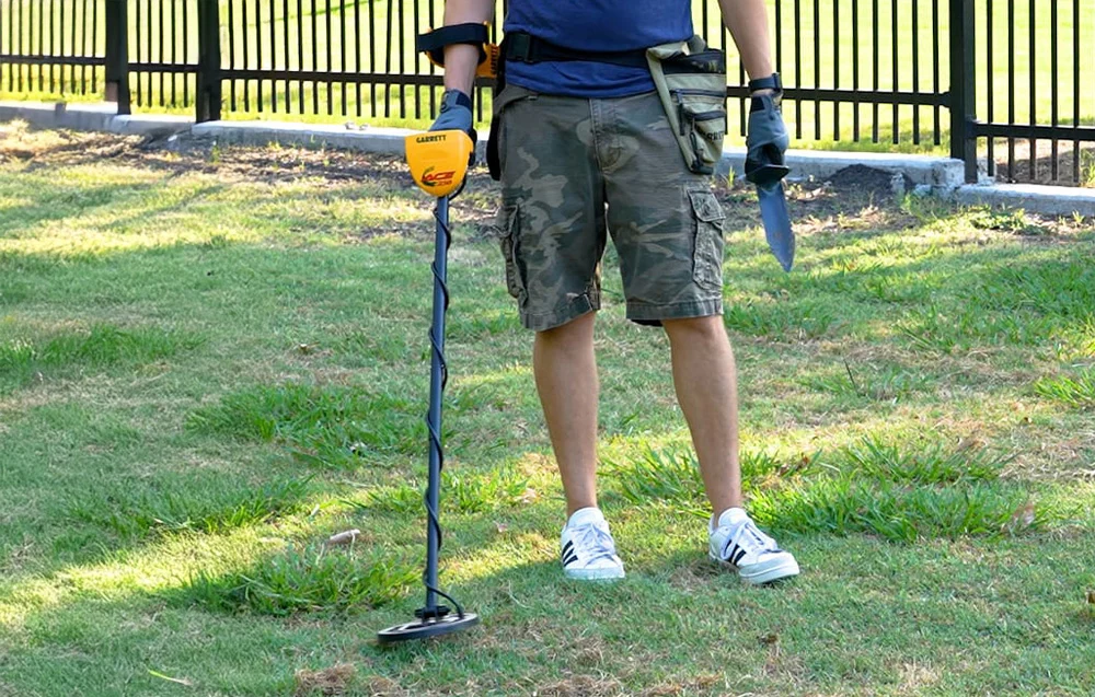 Mężczyzna posługujący się krótką saperką i wskaźnikiem Pinpoint w celu wykopania precyzyjnie monety.