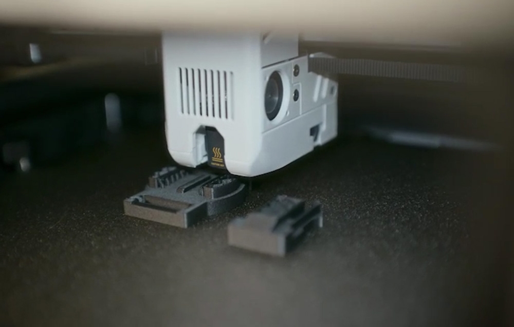 Zbliżenie precyzyjnej głowicy drukarki 3D podczas nakładania warstw modelu na stole roboczym.