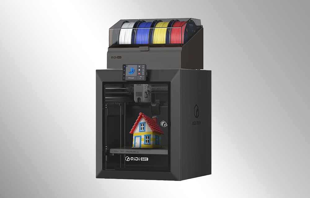 Czarna drukarka 3D QIDI z kolorowymi szpulami filamentu drukująca model małego domu.