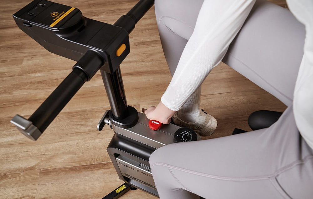Dłoń na czerwonym pokrętle regulacji oporu roweru treningowego KINGSMITH EBW18 W1B
