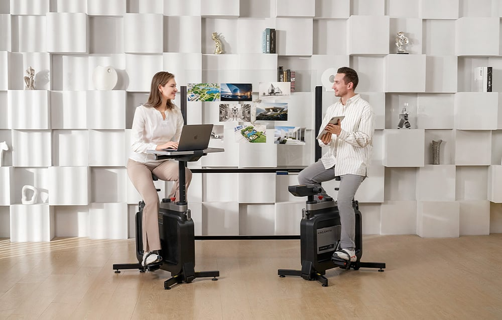 Dwie osoby korzystające z rowerów treningowych KINGSMITH EBW18 W1B przy laptopach